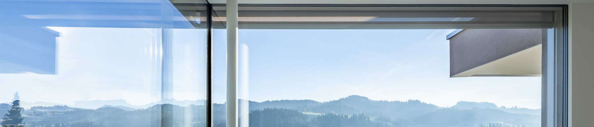 Fully glazed corner comprised of frameless windows, looking out onto an Alpine panorama