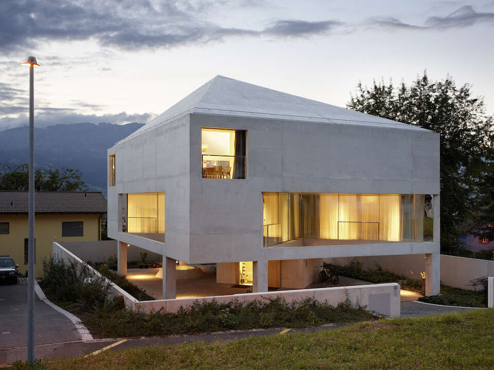 Cubic concrete house standing on pillars, with floor-to-ceiling windows